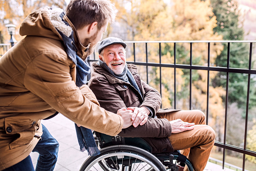 Afbeelding van een verzorger die hand vasthoudt van lachende man in rolstoel. 